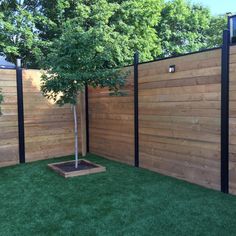 a small tree in a wooden planter next to a fenced in area with grass