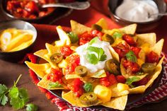 nachos with tomatoes, olives and sour cream on a red tablecloth