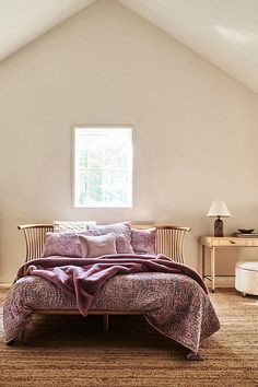 a bed sitting under a window in a bedroom next to a dresser and lamp on top of a rug