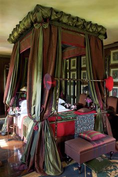 a canopy bed in a bedroom with red and green curtains on the top of it