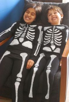 two young children in skeleton costumes laying on a chair with their arms around each other