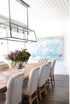 a dining room table with white chairs and a large painting on the wall