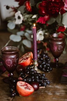 a table topped with candles and fruit next to a vase filled with flowers on top of a wooden table