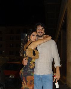 a man and woman standing next to each other in front of a building at night