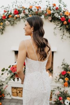 a woman standing in front of an arch with flowers on it and wearing a white dress