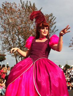 a woman in a pink dress and red hair is dancing on the street while people watch