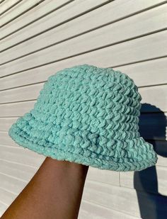 a person's hand holding up a blue crocheted hat on top of a white wall