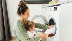 a woman and her daughter are doing laundry in front of the washer that is open