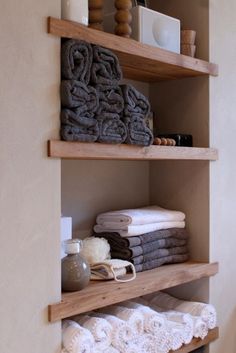 towels are stacked on wooden shelves in the bathroom, with other items sitting on top of them