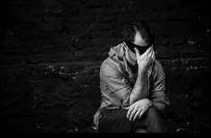 black and white photograph of a man sitting against a brick wall with his hands on his face