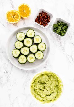 cucumber slices and other ingredients on a white marble countertop with bowls of dips