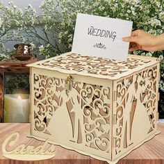 a wooden box with a card in it on a table next to flowers and candles