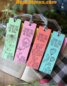 four bookmarks with flowers on them sitting in front of a basket full of books