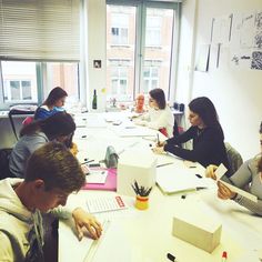 a group of people sitting around a table working on some paper and pencils in an office