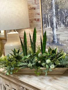 an arrangement of green plants in a wooden container on a fireplace mantel next to a lamp