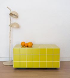 two oranges sitting on top of a yellow box next to a lamp and floor lamp