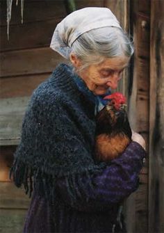 an old woman holding a small chicken in her hands and looking at the camera screen