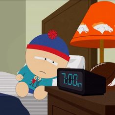 an alarm clock sitting on top of a bed next to a cartoon character wearing a beanie