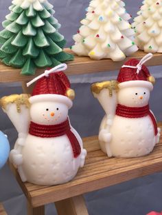 three snowmen sitting on top of a wooden shelf next to christmas trees and other decorations