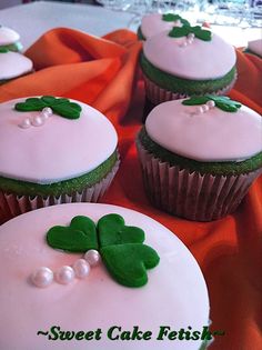 four cupcakes with white frosting and green leaves on top, sitting on an orange cloth