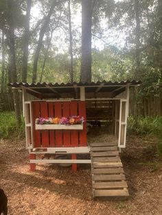 an outhouse in the woods with steps leading up to it and flowers on top