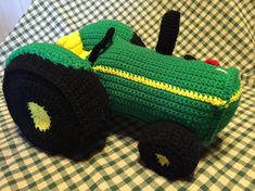 a crocheted green toy tractor sitting on top of a tablecloth covered table