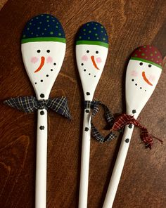 three wooden spoons with snowmen painted on them sitting on top of a table