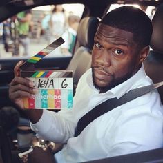 a man sitting in a car holding up a clapstick to his face and looking at the camera