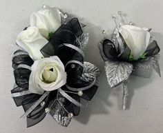 two white roses and black ribbon corsages with silver sequins on them