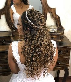 a woman with long curly hair sitting in front of a mirror