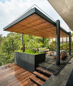 an outdoor living area with wooden decking and plants on the top floor, surrounded by greenery