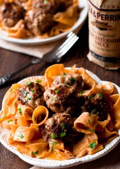 a plate full of pasta and meatballs on a wooden table with a bottle of wine in the background