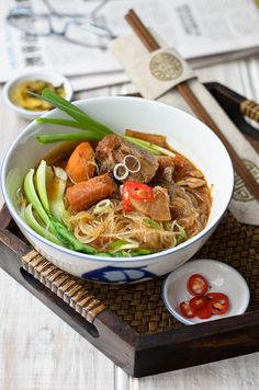 a white bowl filled with meat and vegetables on top of a wooden tray next to chopsticks