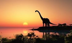 a large dinosaur standing on top of a lush green field next to the ocean at sunset