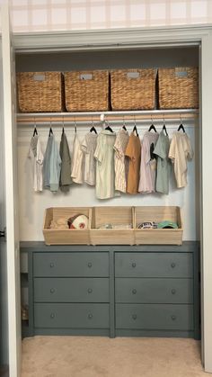 an organized closet with clothes hanging on the wall and baskets in front of it,