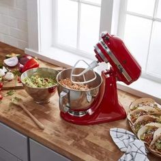 a red stand mixer sitting on top of a wooden counter next to bowls and plates