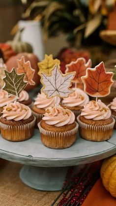 cupcakes with frosting and maple leaf decorations on a cake platter surrounded by fall leaves