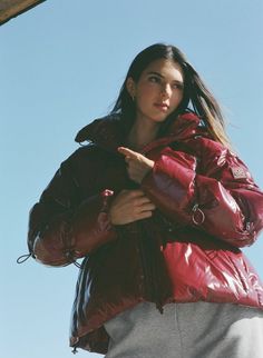 a woman in a red jacket pointing to the side with her hand on her hip