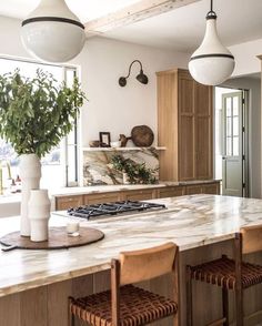 a large kitchen with marble counter tops and wooden chairs in front of an island that has two pendant lights hanging from the ceiling