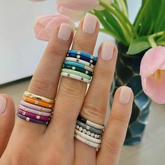 a woman's hand with five different colored rings on her fingers and two pink tulips in the background