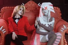 two people dressed in costumes sitting on a red chair with white hair and horns around their heads