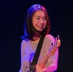 a woman holding a guitar in her right hand and smiling at the camera while standing on stage