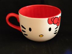 a hello kitty coffee cup is shown on a black surface with red rim and handles