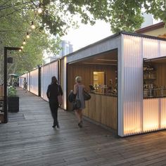 two people walking on a wooden deck next to a building with white walls and windows