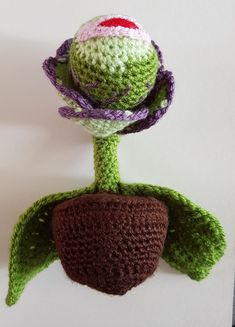 a crocheted green plant with purple and red flowers on it's head