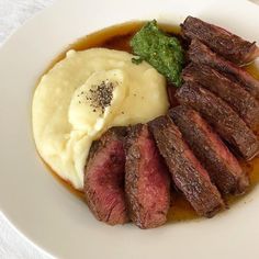 a white plate topped with steak, mashed potatoes and green garnishes