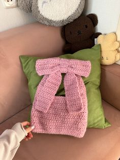 a child's hand holding a crocheted pink blanket over a green pillow