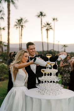 a bride and groom are pouring champagne into glasses on a table with palm trees in the background