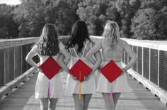 three girls standing on a bridge with their backs to each other wearing graduation caps and gowns