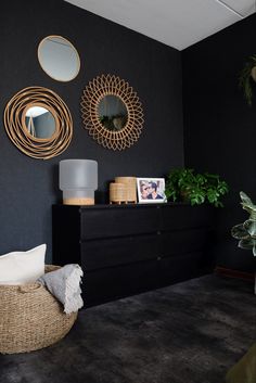 a living room with black walls and gold mirrors on the wall next to a wicker basket